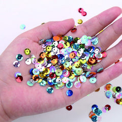 Handful of assorted metallic and iridescent 6mm round cup sequins showing size reference against a hand